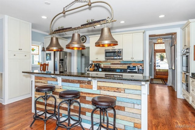 kitchen with dark stone countertops, a kitchen breakfast bar, dark wood-style floors, appliances with stainless steel finishes, and white cabinets