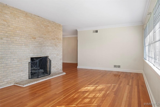 unfurnished living room featuring visible vents, a brick fireplace, wood finished floors, and crown molding