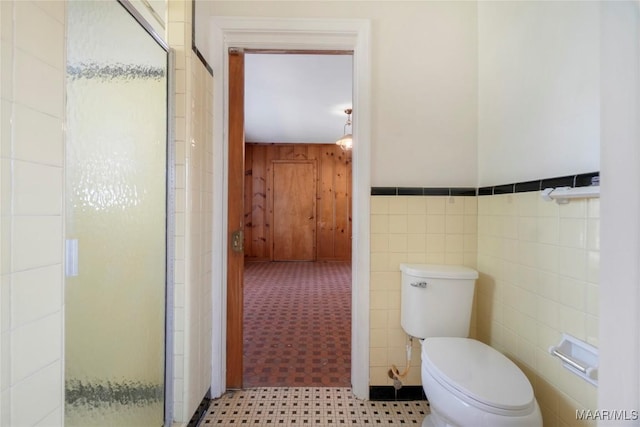 bathroom featuring toilet, tile walls, wainscoting, and a shower stall