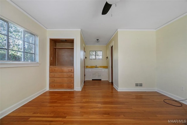 interior space with baseboards, visible vents, light wood finished floors, a sink, and crown molding