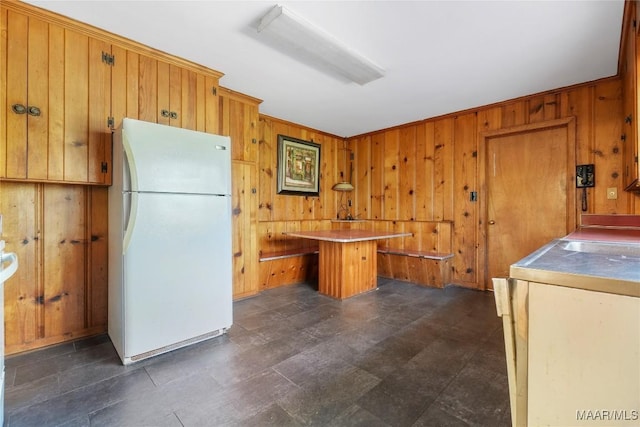 kitchen featuring a kitchen island, freestanding refrigerator, wooden walls, brown cabinetry, and light countertops