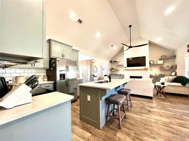 kitchen featuring light wood finished floors, stainless steel fridge with ice dispenser, open floor plan, gray cabinets, and a sink