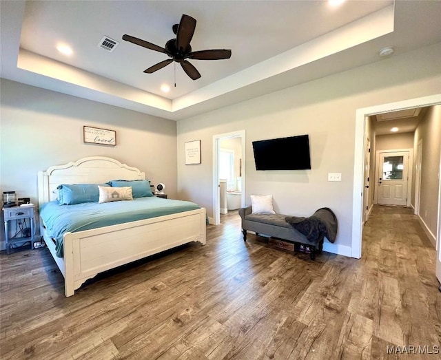 bedroom featuring visible vents, baseboards, a tray ceiling, and wood finished floors