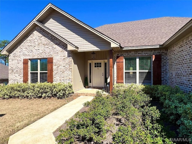 doorway to property featuring brick siding and a shingled roof