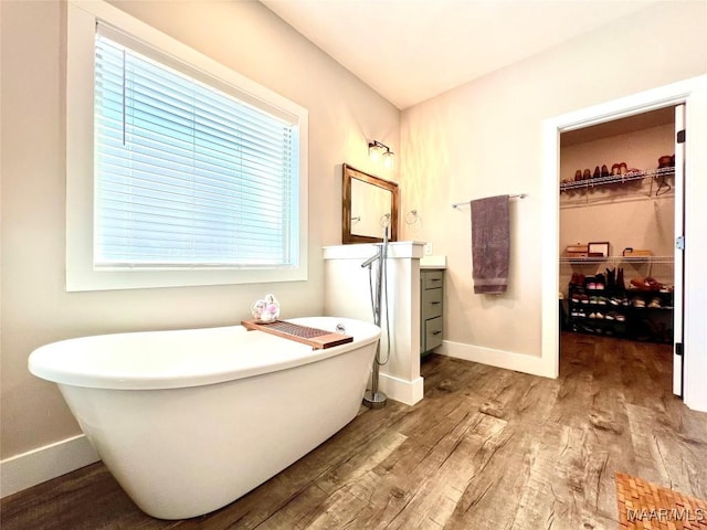 bathroom featuring a spacious closet, baseboards, wood finished floors, a freestanding tub, and vanity