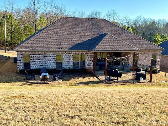 exterior space with a shingled roof, a lawn, brick siding, and a fire pit