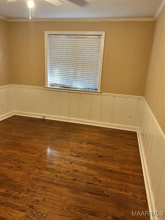 spare room featuring dark wood-style floors, a wainscoted wall, ceiling fan, and ornamental molding