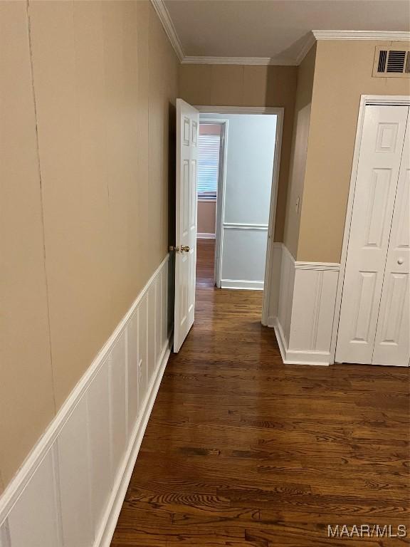 hall featuring a wainscoted wall, visible vents, dark wood finished floors, crown molding, and a decorative wall