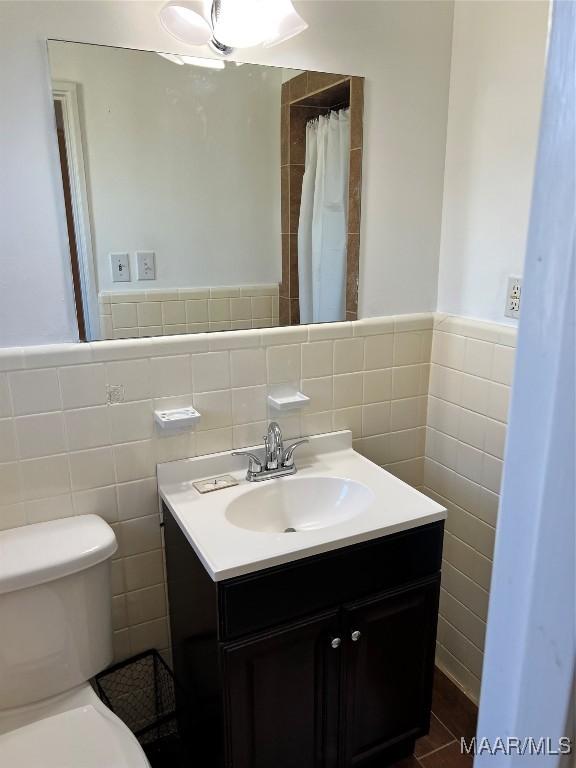 full bathroom featuring toilet, tile walls, wainscoting, and vanity