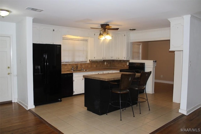 kitchen with visible vents, a kitchen bar, black appliances, tasteful backsplash, and white cabinets