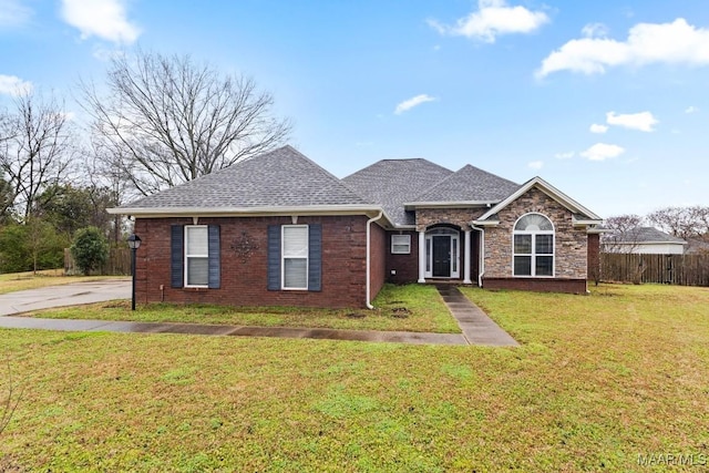 view of front of property featuring brick siding, roof with shingles, a front lawn, and fence