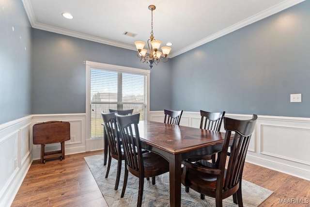 dining room featuring visible vents, a wainscoted wall, ornamental molding, an inviting chandelier, and wood finished floors