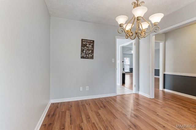 unfurnished dining area with a notable chandelier, baseboards, light wood-type flooring, and a textured ceiling