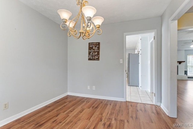 unfurnished room with an inviting chandelier, baseboards, and light wood finished floors