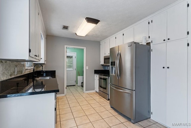 kitchen with dark countertops, decorative backsplash, appliances with stainless steel finishes, white cabinets, and a sink