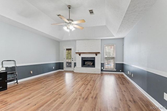 unfurnished living room featuring a tray ceiling, wood finished floors, visible vents, and baseboards