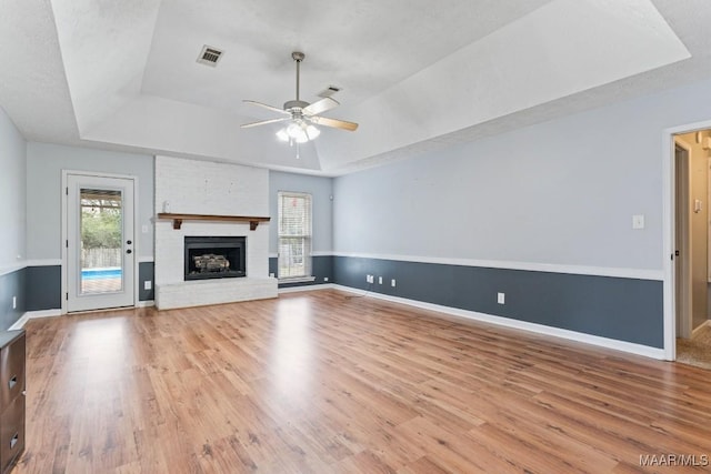 unfurnished living room with visible vents, a fireplace, a raised ceiling, and wood finished floors