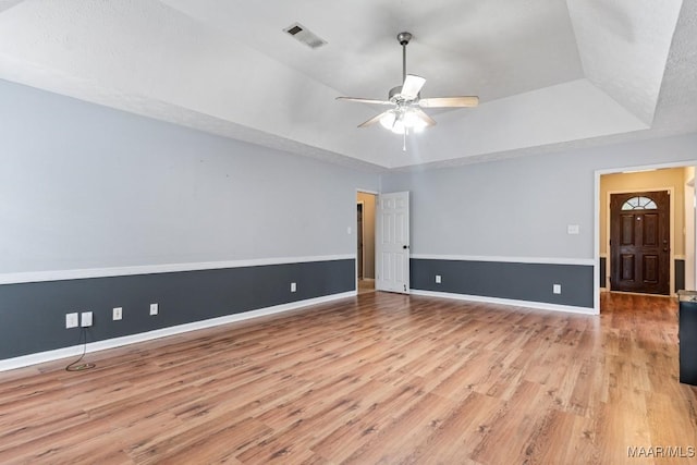 spare room with a ceiling fan, wood finished floors, visible vents, baseboards, and a raised ceiling