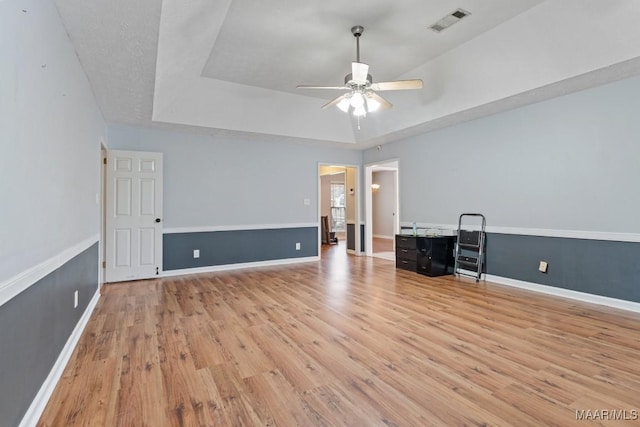 unfurnished room with baseboards, visible vents, light wood finished floors, ceiling fan, and a raised ceiling