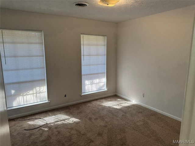 carpeted spare room featuring baseboards, visible vents, and a textured ceiling