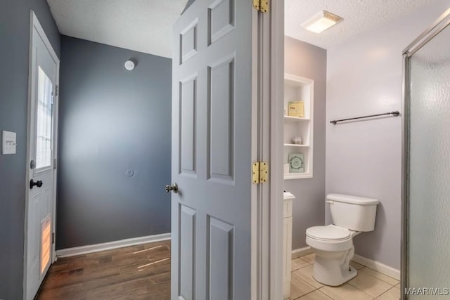 bathroom with baseboards, toilet, a shower with shower door, wood finished floors, and a textured ceiling