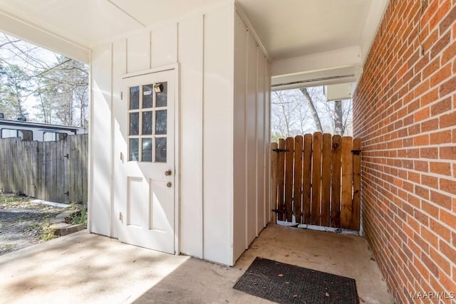 entrance to property featuring a gate, brick siding, board and batten siding, and fence