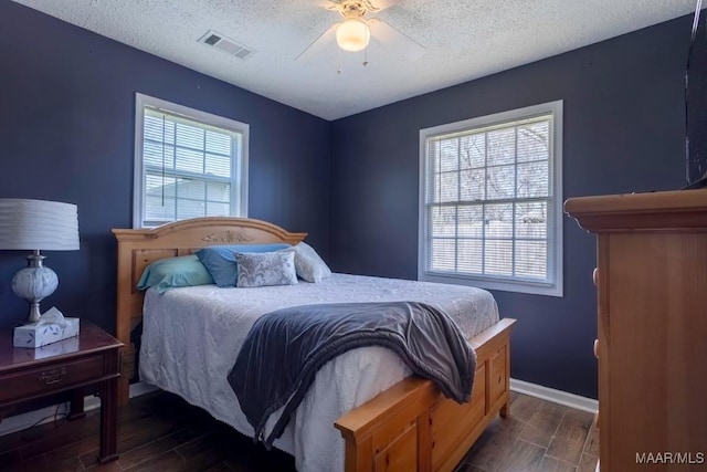 bedroom with visible vents, a textured ceiling, wood finished floors, baseboards, and ceiling fan