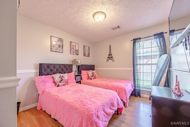 bedroom featuring visible vents, multiple windows, a textured ceiling, and wood finished floors