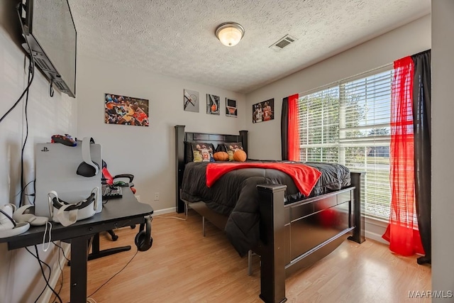 bedroom featuring baseboards, light wood-style floors, visible vents, and a textured ceiling