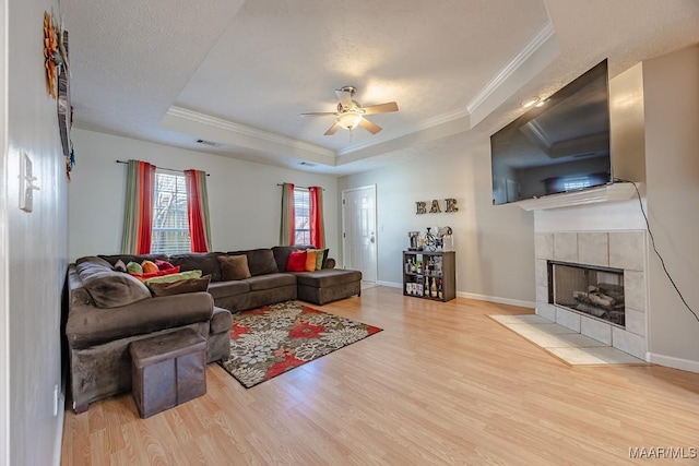 living room featuring visible vents, a tray ceiling, wood finished floors, a fireplace, and crown molding