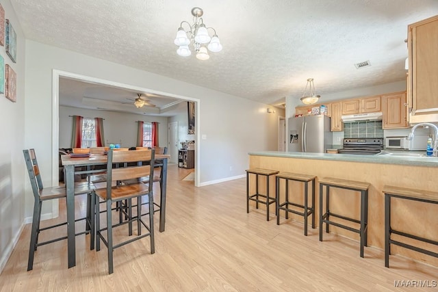 kitchen featuring visible vents, light brown cabinetry, under cabinet range hood, appliances with stainless steel finishes, and a raised ceiling