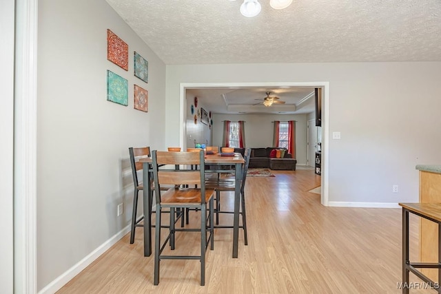 dining space with light wood finished floors, baseboards, and a tray ceiling