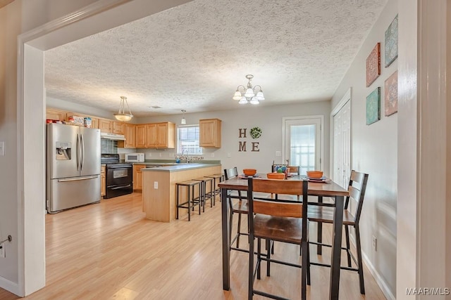 dining space featuring an inviting chandelier, a textured ceiling, light wood-type flooring, and baseboards