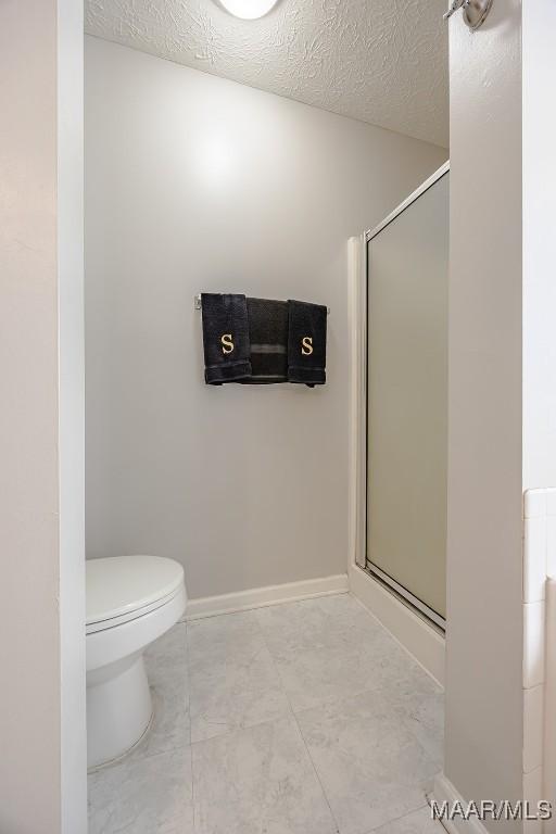 bathroom featuring a shower stall, toilet, baseboards, and a textured ceiling