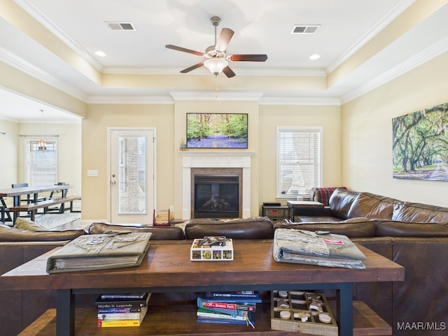 living area with a raised ceiling, a ceiling fan, visible vents, and a premium fireplace