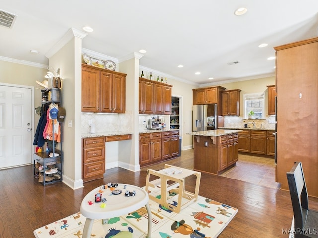 kitchen featuring brown cabinetry, visible vents, stainless steel fridge with ice dispenser, and built in desk