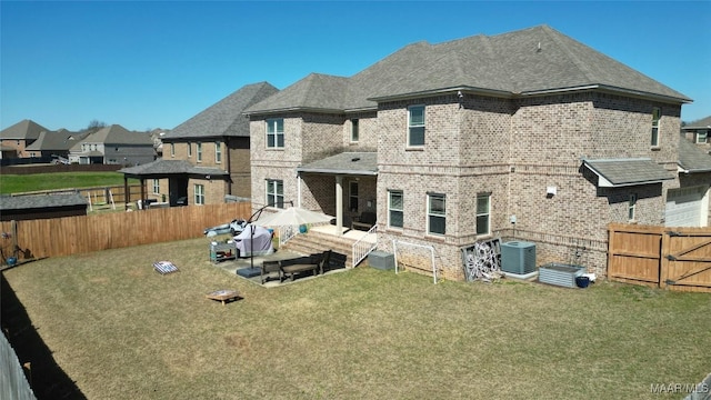 back of property with central AC unit, brick siding, a fenced backyard, and a lawn