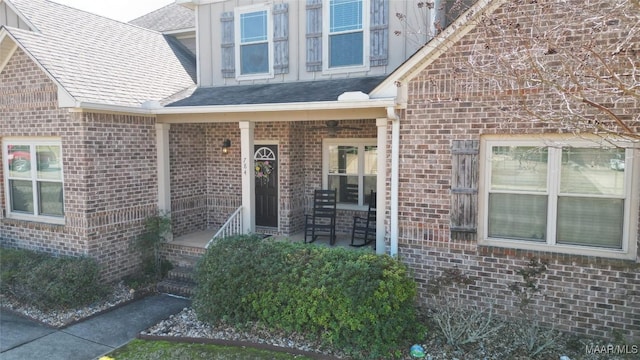 property entrance featuring brick siding, covered porch, and a shingled roof