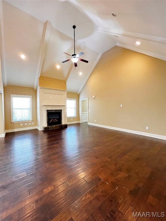 unfurnished living room featuring baseboards, dark wood finished floors, a fireplace with raised hearth, ceiling fan, and vaulted ceiling