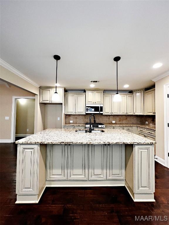 kitchen with light stone countertops, a large island with sink, ornamental molding, a sink, and stainless steel microwave