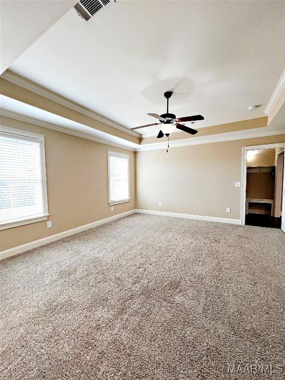 empty room featuring visible vents, crown molding, baseboards, carpet, and a raised ceiling