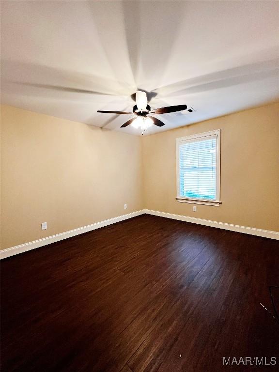 spare room with dark wood finished floors, a ceiling fan, and baseboards