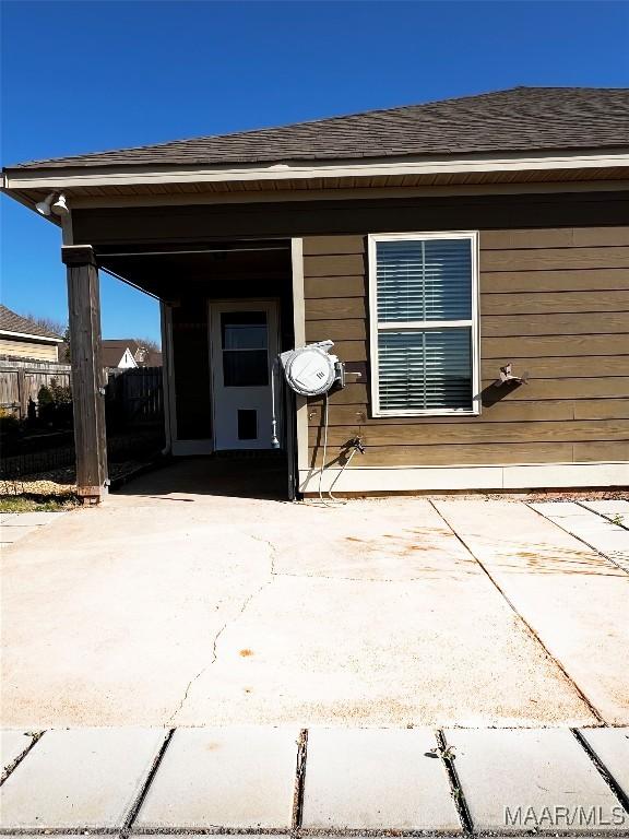 entrance to property featuring roof with shingles and fence