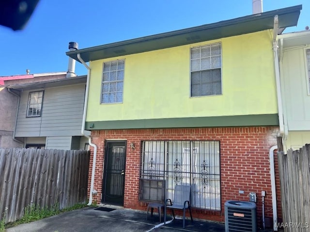 back of house with cooling unit, brick siding, stucco siding, and fence