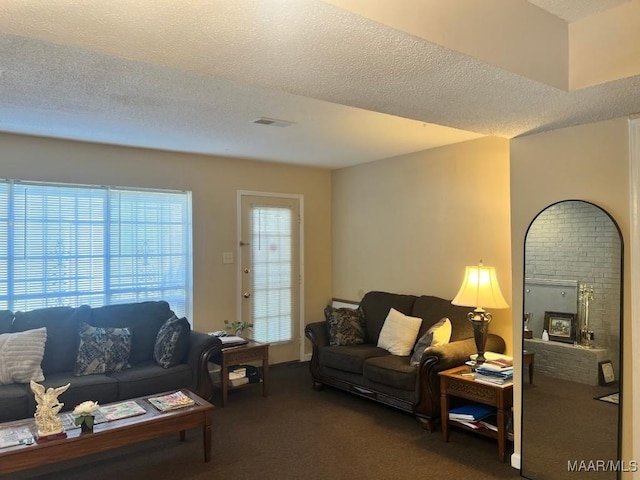 living area with visible vents, carpet flooring, a brick fireplace, and a textured ceiling