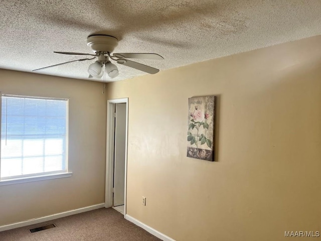 carpeted empty room with visible vents, ceiling fan, a textured ceiling, and baseboards