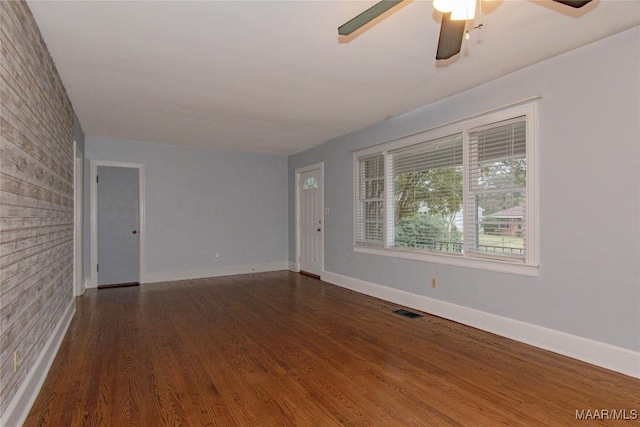 empty room with wood finished floors, visible vents, brick wall, and baseboards