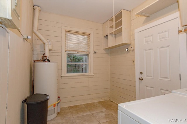 washroom featuring water heater, separate washer and dryer, wood walls, light tile patterned floors, and laundry area