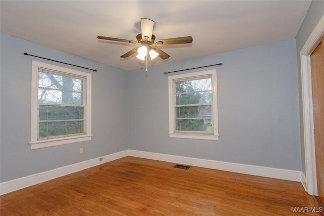 empty room with visible vents, a healthy amount of sunlight, baseboards, and wood finished floors