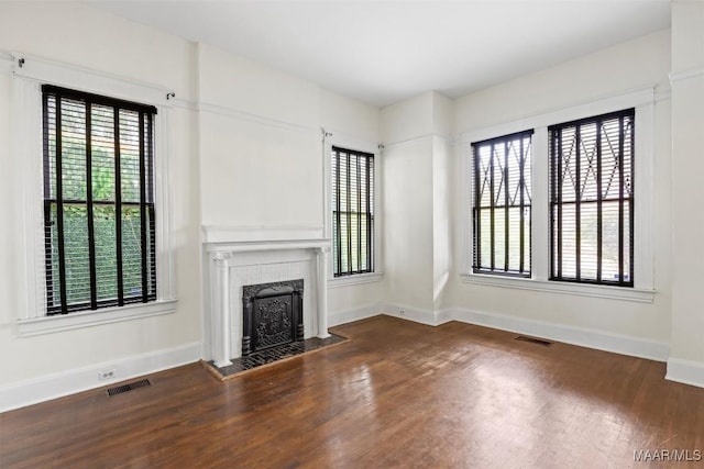 unfurnished living room featuring a tiled fireplace, a wealth of natural light, visible vents, and wood-type flooring